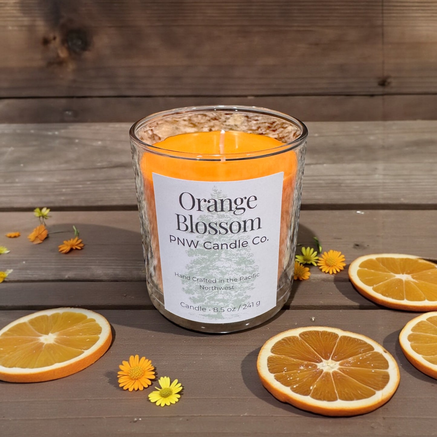PNW Candle Co orange blossom scented candle in a glass jar with a lit wick, showcasing its bright orange color and floral aroma.