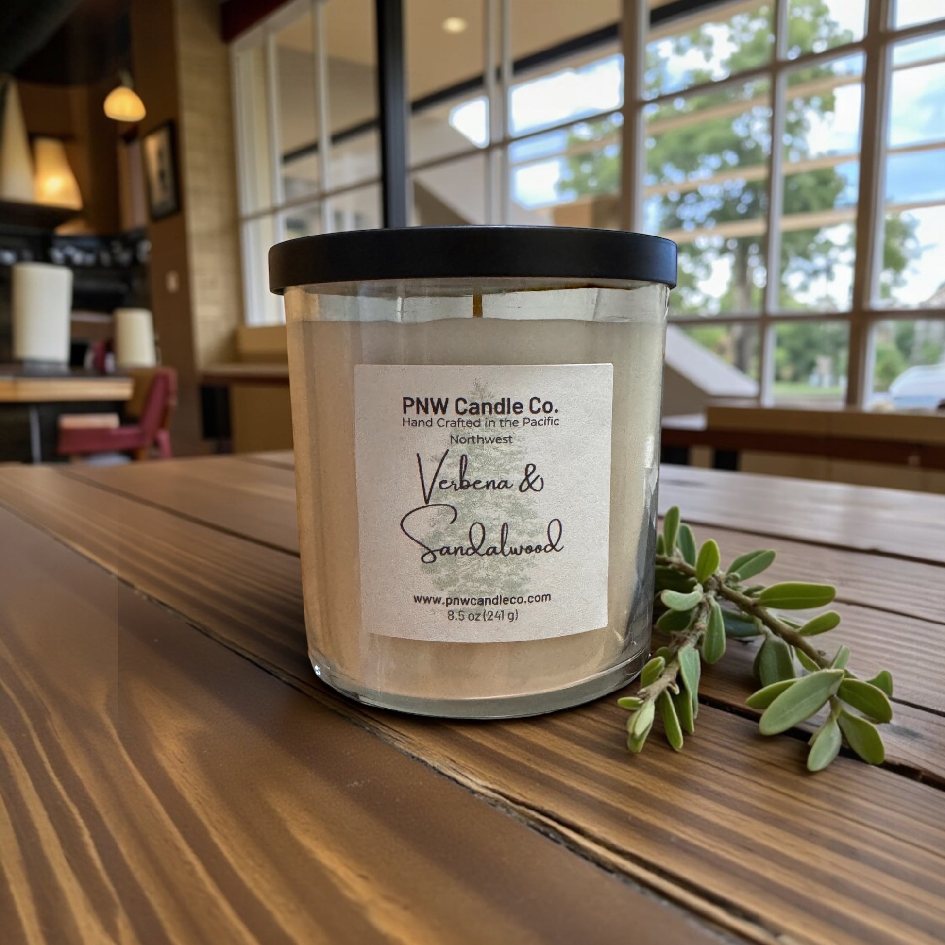 PNW Candle Co scented candle with verbena and sandalwood aroma, featuring a natural wax container and a lit wick.