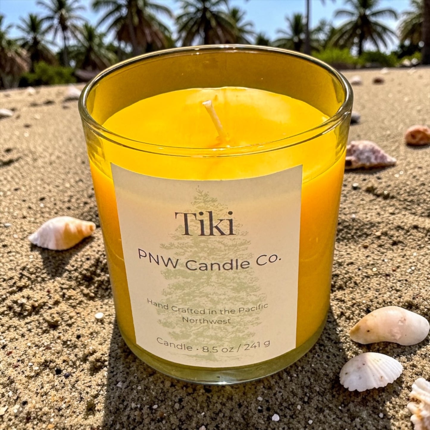 PNW Candle Co Tiki Scented Candle in a glass jar with a lit wick, showcasing warm candlelight and tropical-inspired design.