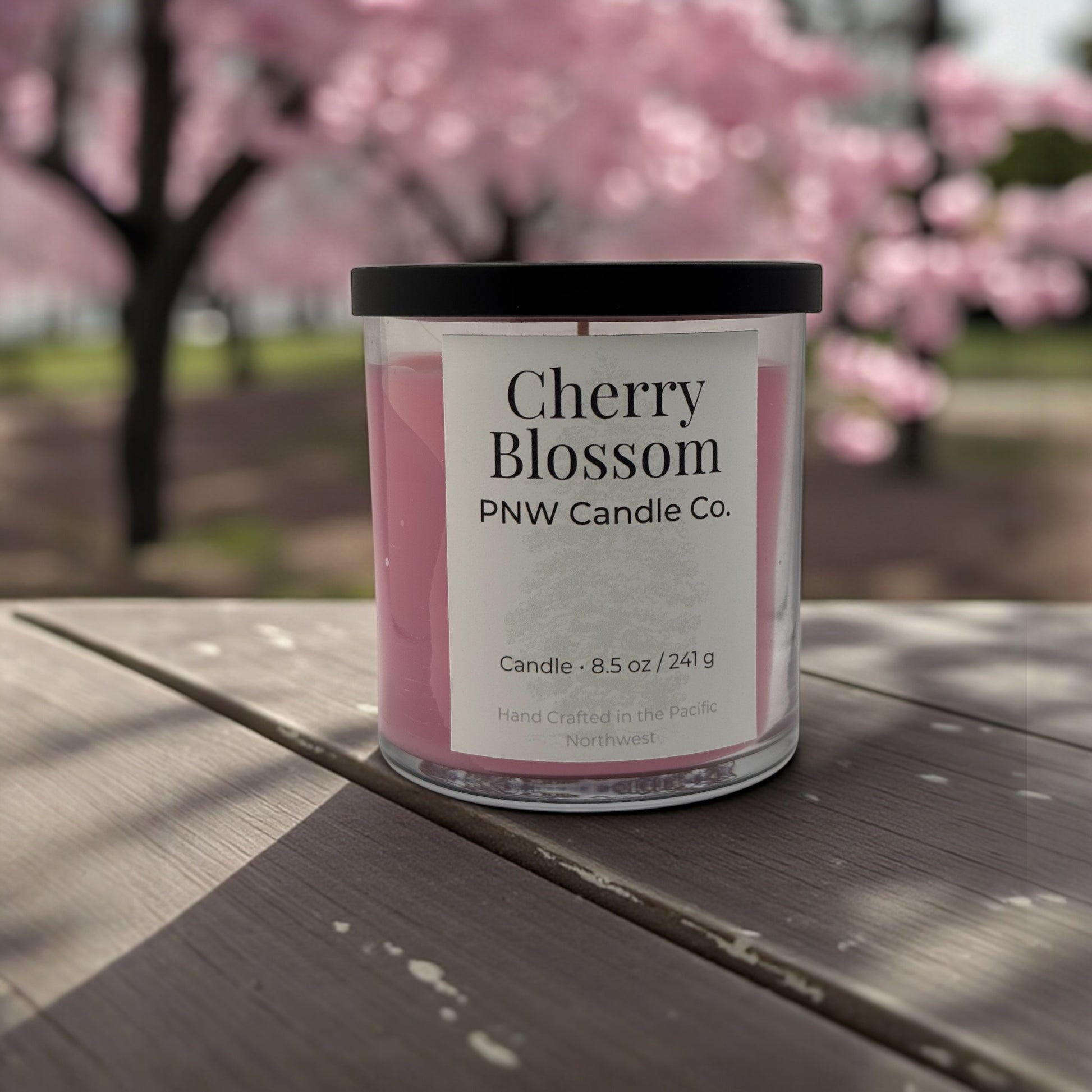 Cherry Blossom scented candle by PNW Candle Co, featuring a sleek glass jar with a lit wick and soft floral design.