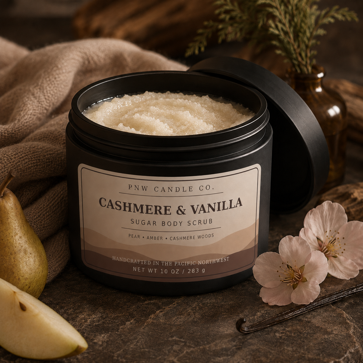 Cashmere & Vanilla 10 oz sugar scrub in a matte-black jar with pear, vanilla bean, blossoms, and warm cashmere.