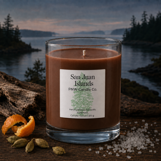 San Juan Islands scented candle by PNW Candle Co with rich brown wax beside cardamom, orange peel, and sea salt in a Pacific Northwest island scene.