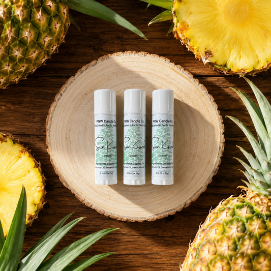 Three Sun Kissed Lip Balm tubes by PNW Candle Co displayed with fresh pineapple on a rustic wood background.